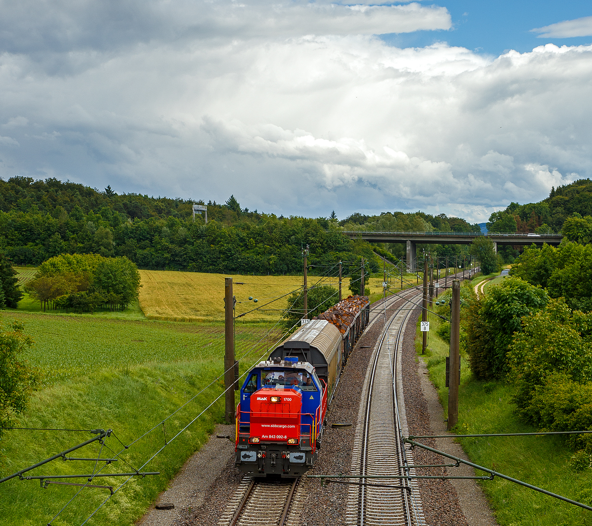 Die SBB Cargo Am 843 092-8 (eine modifizierte Vossloh MaK 1700) fährt am 17.06.2016 mit einem kurzen Güterzug durch Bietingen in Richtung Schaffhausen. 

Einen lieben Gruß an den freundlichen Lokführer zurück.

Die Lok wurde 2005 von Vossloh in Kiel unter der Fabriknummer 1001440 gebaut und an die SBB Cargo AG in Basel geliefert. Sie gehört zu den letzten fünf Loks der Serie an die SBB Cargo, diese fünf Maschinen (Am 843 091 bis 095) sind zusätzlich mit der deutschen Zugsicherung Indusi ausgerüstet worden und haben einen zweiten Führerstand auf der rechten Seite. 

Die SBB Am 843 ist eine moderne Rangier- und Güterzugslokomotive der Schweizerischen Bundesbahnen (SBB). Sie ersetzt ältere Rangierlokomotiven wie die SBB Bm 4/4 und SBB Bm 6/6. Eingesetzt wird die Am 843 von der Division Infrastruktur (843 001ff), der Division Personenverkehr (041ff) und von SBB Cargo (050ff). Die Division Infrastruktur verwendet die Am 843 vor allem in den grossen Rangierbahnhöfen, Personenverkehr in Basel und Chiasso und bei SBB Cargo dient sie vor allem für Zustellfahrten im Nahgüterverkehr.

Die Am 843 verfügt über einen Mikropartikelfilter und gilt als eine der saubersten Diesellokomotiven. Die Filteranlage verhindert, dass 95 % der Russpartikel in die Umwelt abgegeben werden. Die Am 843 basiert auf den dieselhydraulischen Standardlokomotiven des Typs G 1700-2 BB des Kieler Schienenfahrzeugherstellers Vossloh, ist aber im Gegensatz zur Standard-Version auf den in der Schweiz üblichen Linksverkehr ausgelegt.

Anfang der 2000ter musste eine neue Lokomotive angeschafft werden, welche allen Anforderungen gerecht wurde. So musste die Lok über hervorragende Langsam Fahreigenschaften verfügen um im Verschubdienst eingesetzt werden zu können. Die SBB-Cargo wollte aber auch im Nahbereich Zustellfahrten machen, was eine Höchstgeschwindigkeit von 100 km/h erfordernde und gute Leistung. Schließlich fiel die Wahl auf die MaK 1700 BB, welches bei Vossloh in Kiel entstehen sollte. Vossloh entstand aus der ehemaligen und bekannten Unternehmen Maschinenfabrik Kiel (MaK). Dies war die erste größere Serie die der Kieler Lokomotivbau in die Schweiz verkaufen konnte. Noch bei der letzten Ausschreibung haben die Kieler gegen das Konsortium um Alstom verloren. Ebenfalls eine Neuheit war, dass die SBB erstmals eine größere Anzahl dieselhydraulischer Lokomotiven anschafften, nachdem bei der Am 841 noch einer dieselelektrischen Lokomotive der Vorzug gewährt wurde.

Der Lokrahmen besteht aus Walzträgern und massiven Blechen, welche in Schweißkonstruktion miteinander verbunden wurden. Dadurch entsteht ein stabiler und robuster Grundaufbau, welcher der Lok die notwendigen Festigkeiten verleiht. Im Lokrahmen wurde eine so genannte Umweltwanne montiert, welche aus dem Fahrmotor austretenden Flüssigkeiten (Mineralölen und Wasseremulsionen) auffängt, diese können mit Hilfe eines Ablasshahnes entleert und fachmännisch entsorgt werden.

Der vordere längere Vorbau beinhaltet neben dem Dieselmotor auch die notwendige Kühlanlage und das Antriebsgetriebe. Der kürzere hintere Vorbau enthält neben der Druckluftanlage auch die elektrischen Komponenten wie die Batterieladung.

Zwischen den beiden Vorbauten befindet sich das Mittelführerhaus, welches über die zwei diagonal gegenüberliegenden Eingangstüren betreten werden kann. In ihm sind alle für den Lokführer notwendigen Einbauten vorhanden. Ein Führersitz je Fahrpult und Fahrrichtung, welcher mit Arm- und Rückenlehnen ausgerüstet ist, erlaubt die sitzende Bedienung der Lokomotive. Dieser Führersitz ist drehbar gelagert und kann zusammengeklappt und unter den Führertisch verschoben werden. Dadurch ist auch die stehende Bedienung der Lokomotive ohne Behinderung möglich. Zur Entlastung der Füße sind auch verstellbare Fußstützen montiert. Der Fußboden ist mit einem Profilgummibelag belegt worden, der eine einfache Reinigung und dennoch einen guten Stand erlaubt.

Angetrieben wird die Lokomotive von einem 12-Zylinder-4Takt-Dieselmotor vom Typ Caterpillar 3512 B DI-TA-SCAC, dieser erbringt mit Hilfe der beiden Abgasturbolader und der Ladeluftkühlung eine maximale Leistung von 1.500 KW (2.040 PS). Seine höchste Drehzahl beträgt 1.800 U/min. Er wird mit Hilfe eines elektrischen Anlassers gestartet und ist elektronisch geregelt. Dadurch ist es möglich, den Motor bestmöglich im optimalen Leistungsbereich zu betreiben. Sein Gewicht beträgt mit 322 Liter Schmieröl und 134 Liter Kühlwasser 7.700 kg.

Die vom Dieselmotor erzeugte Leistung wird mittels einer Gelenkwelle auf das hydrodynamische Getriebe (Turbowendegetriebe), vom Typ Voith L5r4zseU2, übertragen. Das Getriebe hat eine maximale Leistung von 1.400 kW. Es beschränkt somit die Leistung der Lokomotive und verhindert zugleich, dass der Fahrmotor überlastet werden kann. Seine maximale Drehzahl ist gleich groß, wie jene des Fahrmotors. 

Das Turbowendegetriebe besitzt für jede Fahrrichtung zwei Drehmomentwandler. Dem eigentlichen Wandlergetriebe ist eine mechanische Getriebe nachgeschaltet, das eine niedrige für den Rangierbetrieb bestimmte Schaltung und eine höhere für den Streckenbetrieb bestimmte Schaltung zur Verfügung zu stellen. Diese Umschaltung darf jedoch erst im Stillstand erfolgen.

Die Achsen in den Drehgestellen werden über Gelenkwellen vom Turbowendegetriebe angetrieben. Die Übertragung auf die Achsen erfolgt mit Hilfe von Stirnradgetrieben mit Kegelradvorgelege.

Technische Daten:
Spurweite: 1.435 mm (Normalspur)
Achsformel: B'B'
Länge über Puffer: 15.200 mm
Höhe: 4.220 mm
Breite: 3.080 mm
Drehzapfenabstand: 7.700 mm
Achsstand im Drehgestell: 2.400 mm
Dienstgewicht:  80 t
Höchstgeschwindigkeit: 100 km/h (40 km im Rangiergang)
Installierte Leistung: 1.500 kW (2.040 PS)
Anfahrzugkraft:  249 kN
Treibraddurchmesser:  1.000 mm
Motorentyp:  Caterpillar 3512B DI-TA-SCAC
Nenndrehzahl: 1.800/min
Kleinster bef. Halbmesser:  60 m
Tankinhalt: 3.500 l