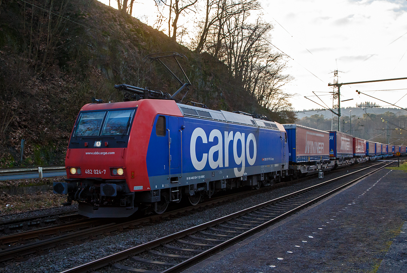 Die an die SBB Cargo International AG vermietete SBB Cargo Re 482 024-7 (91 85 4482 024-7 CH-SBBC) fährt am 28.01.2023 mit einem „Winner“ KLV-Ganzzug durch Scheuerfeld (Sieg) in Richtung Siegen.

Die TRAXX F140 AC1 wurde 2003 von Bombardier in Kassel unter der Fabriknummer 33590 gebaut und an die SBB Cargo AG geliefert. Sie hat die Zulassungen für die Schweiz und Deutschland. Wobei durch das fehlende ETCS ist der Einsatz in der Schweiz nur bedingt möglich, so sieht man sie hauptsächlich in Deutschland auf der Strecke zwischen Köln und Basel. Einige SBB Cargo Re 482 sind auch bereits verkauft worden.
